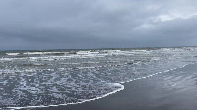 Fast moving alone grey sand beach coastline with waves and cloudy sky 
