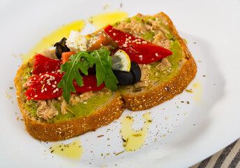 Healthy toasts with guacamole, canned tuna, feta cheese, fresh vegetables and lemon served on white plate..