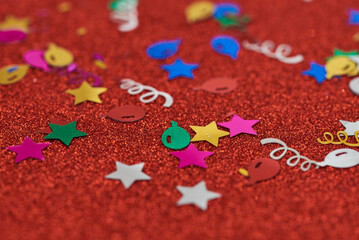 Colourful confetti on red glitter surface.