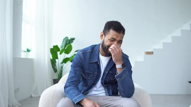 African American man watches TV at home and shows disgust, the guy watches a nasty video and covers his nose from the bad smell
