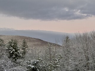 Windham ski town in Catskill Mountains at golden hour sunrise. Fresh, white snow blankets the landscape and trees. Pink and blue clouds in early morning. Mountain slope in distance. Scenic view.