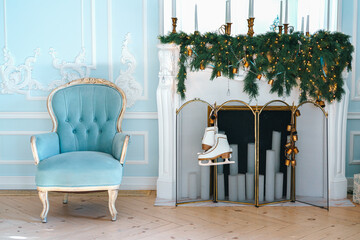 Christmas decorated living room features blue upholstered vintage chair, decorated fireplace with green garlands and twinkling lights and hanging ice skates. The ambiance is tranquil and festive.
