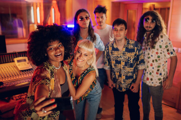 Diverse group of musicians taking selfies at music recording studio.