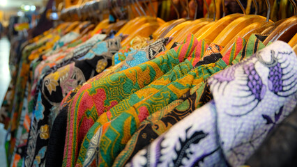 A close-up shot of colorful batik shirts hanging on wooden hangers in a market stall