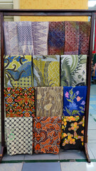 Colorful batik fabrics displayed on a wooden rack. Close-up shot highlights intricate patterns and vibrant colors. Perfect for fashion blogs or promoting Indonesian culture