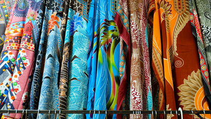 Colorful batik fabrics hanging on a rack. Close-up shot highlights intricate patterns and vibrant colors. Perfect for fashion blogs or promoting Indonesian culture.