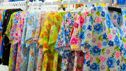 A colorful display of floral print blouses hanging on a rack in a clothing store. The image uses a close-up technique to focus on the vibrant colors and intricate patterns of the blouses