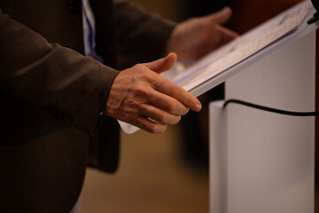 focus sur un micro et les mains d'un orateur prononçant un discours à la tribune lors d'un meeting politique, d'un colloque ou d'une réunion	