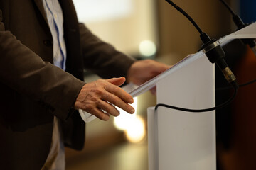 focus sur un micro et les mains d'un orateur prononçant un discours à la tribune lors d'un meeting politique, d'un colloque ou d'une réunion	