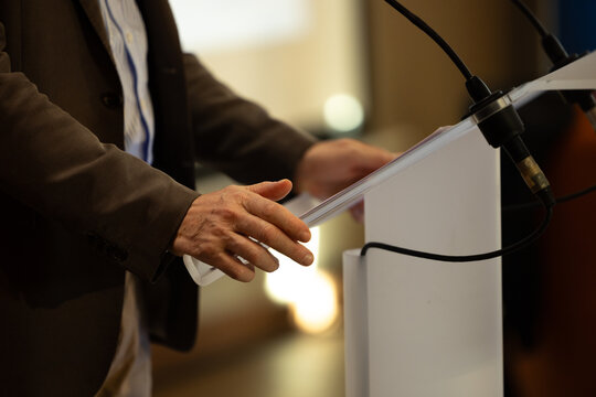 focus sur un micro et les mains d'un orateur pronon&ccedil;ant un discours &agrave; la tribune lors d'un meeting politique, d'un colloque ou d'une r&eacute;union	
