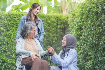 asian senior woman on wheelchair hands holding a female physiotherapist in hijab,a daughter standing behind her,health care worker empowering patient or better health