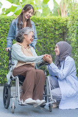 asian senior woman on wheelchair hands holding a female physiotherapist in hijab,a daughter standing behind her,health care worker empowering patient or better health