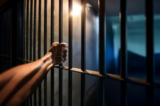 Man's hand gripping the bars of cell in prison. Punishment, and captivity concept.