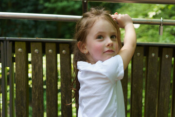 Fototapeta premium Beautiful cheerful girl in a white T-shirt having fun in the summer outdoors. Concept of an active, mobile, sincere child