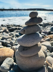 Balancing stones by the shore.
A stack of smooth, balanced stones rests peacefully on a pebble-covered shore, with a shimmering river and distant horizon in the background.