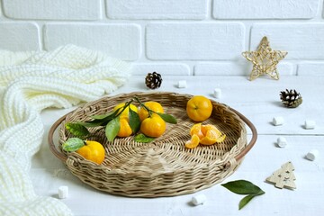 Wicker tray with tangerines on white wooden table. Cozy winter composition.