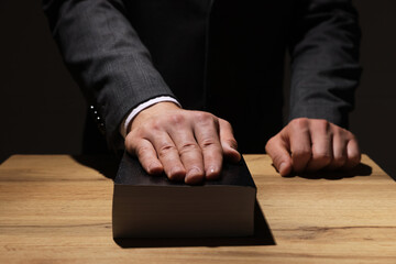 Man taking oath with his hand on Bible at wooden table, closeup