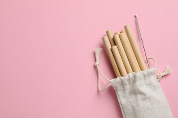 Bamboo drinking straws and cleaning brush in bag on pink background, top view. Space for text