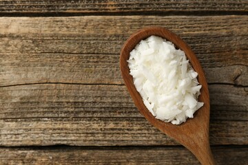 White soy wax flakes in spoon on wooden table, top view. Space for text