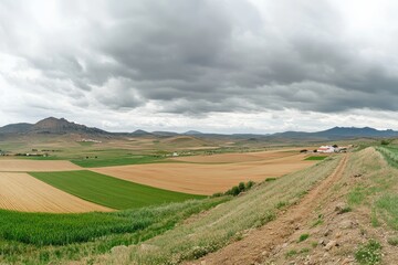 Obraz premium Expansive Agricultural Landscape under Dramatic Cloudy Sky with Rolling Hills, Vibrant Fields, and Rustic Farmhouse Imagery