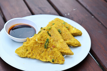 Deep fried tempeh or Tempe mendoan goreng made from soy bean with flour batter and spring onion on white plate. street food. Fried tempe served on the white plate with chilli sauce and ketchup.