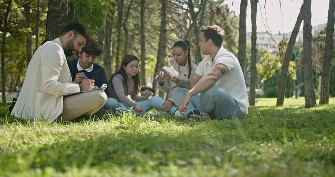 A group of diverse high school friends gathers in a sunny park for lunch, sharing food, laughter, and lively conversation while enjoying their break together.
