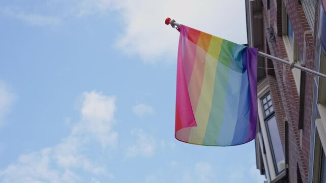 Lgbtq pride flag waves against blue sky by historic brick building