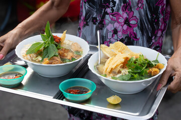 Vietnamese Pho noodle soup typical breakfast for two beautifully presented on a silver tray and being delivered in the street. Dishes are "Hu Tiu" and "Banh Pho."