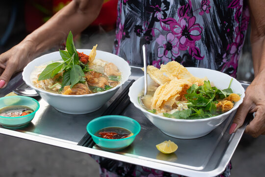 Vietnamese Pho noodle soup typical breakfast for two beautifully presented on a silver tray and being delivered in the street. Dishes are "Hu Tiu" and "Banh Pho."