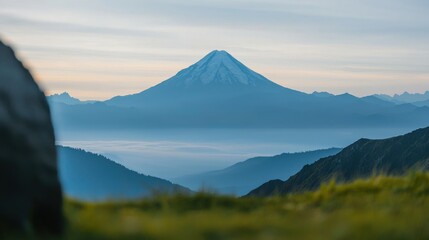Fototapeta premium A majestic volcano rises above misty valleys, surrounded by lush green hills under a soft, pastel sky at dawn.