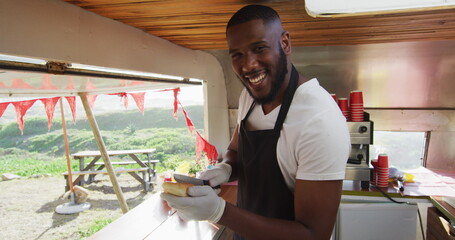 Portrait of african american man smiling while preparing hot dogs in the food truck