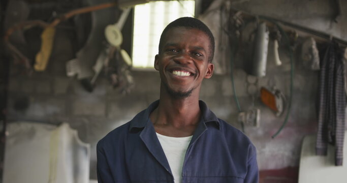 Portrait of a happy African male panel beater in a township workshop, looking at camera and smiling,
