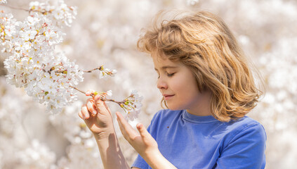 Cute blonde kid boy in spring garden. Little child under a blossom tree. Happy kid playing under blooming cherry tree. Kid with flower on Easter. Adorable kid in blooming cherry garden on spring day.