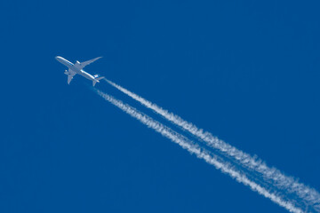 Commercial airplane with jet stream overhead view with blue background and vapour trail.