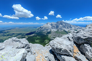Panoramic mountain vista with rocky foreground, blue sky, and fluffy clouds.