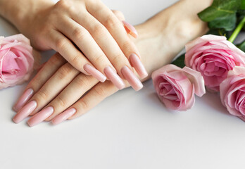 Woman showing her beautiful pastel pink manicure near pink roses