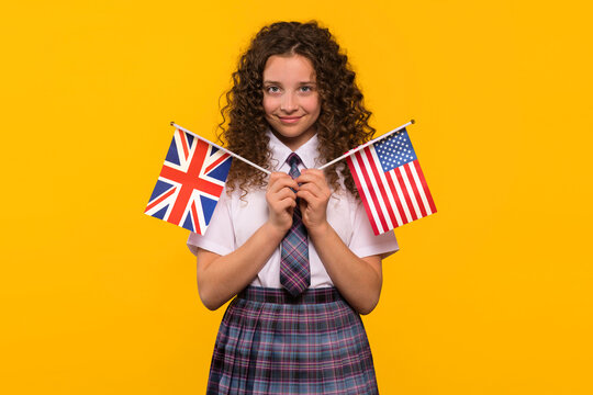 Smiling girl holding USA and UK flags, posing in school uniform. Language difference between British and American English. To advertise a language school
