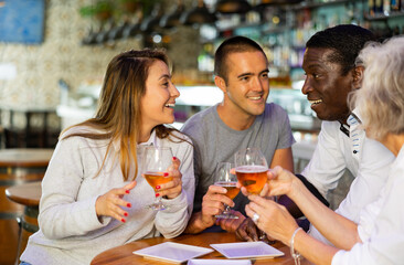 Mixed age range people celebrating holiday together in beer pub, toasting with drinks. Selective focus on people