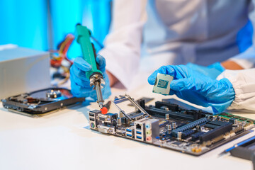 Close-up of a technician wearing gloves soldering electronic components at a desk in an office. The scene highlights precision, technical expertise, and focused work in an electronics lab setting