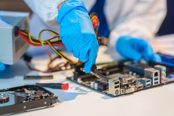 Close-up of a technician wearing gloves soldering electronic components at a desk in an office. The scene highlights precision, technical expertise, and focused work in an electronics lab setting
