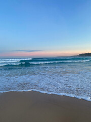 Bondi Beach, Australia, twilight sunset over ocean, blue rolling waves, pink clouds, beige sand