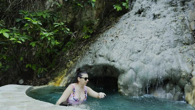 Woman enters an infinity pool with thermal waters, waterfall and natural cave at La Gloria Tolantongo spa resort, Mexico