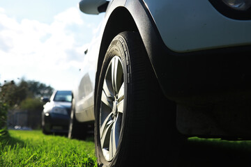 Close-Up of Car Wheel Parked on Grass with Another Car in the Background