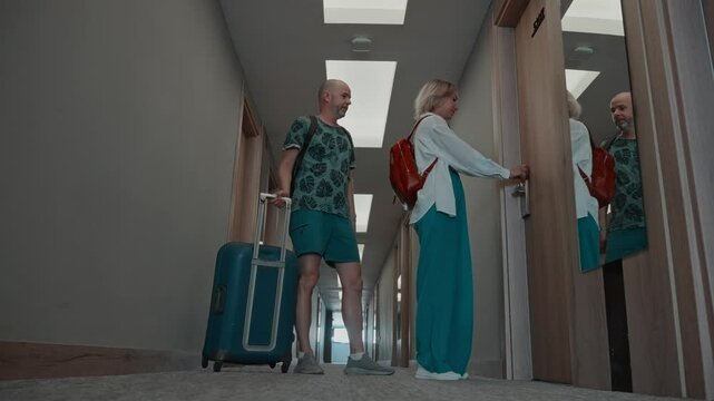 A married couple on vacation at a hotel. A man and a woman are walking along the corridor with a suitcase. Joyful people check in to the hotel room.