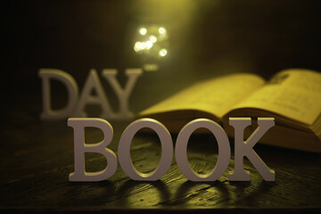 Open Book with DAY and BOOK Letter Decor on Wooden Table under Warm Light