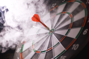 Red Dart Hitting Bullseye on Smoky Dartboard, Precision and Accuracy in Focus