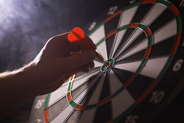 Hand Aiming Dart at Bullseye on Dartboard in Smoky Atmosphere