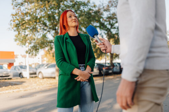 Journalist interviewing businesswoman with red hair holding microphone outdoors