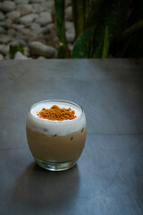 iced sea salt coffee in a curved transparent glass, with brown sugar toppings, placed on concrete surface