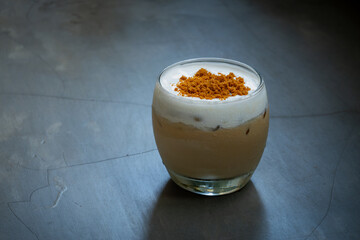 iced sea salt coffee in a curved transparent glass, with brown sugar toppings, placed on concrete surface